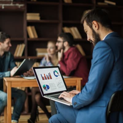 Der Finanzmanager der Geo-Sichtbarkeit haben will, arbeitet am Laptop an den Marketinggrafiken vor dem Hintergrund des Arbeitsbereichs des Geschäftsteams im Büro.