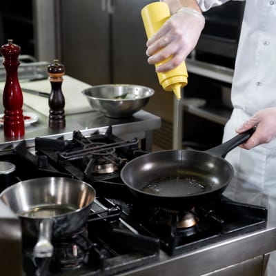 Der Koch gießt Olivenöl aus einer Flasche in eine Pfanne