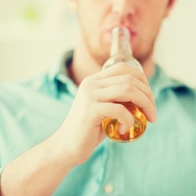 Konzept: Getränke, Entspannung, Freizeit und Menschen – Nahaufnahme eines Mannes, der zu Hause auf dem Sofa sitzt und alkoholfreies Bier trinkt