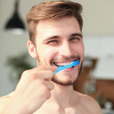 Junger Mann mit braunen Haaren, putz dich mit einer blauen Zahnbürste die Zähne. 