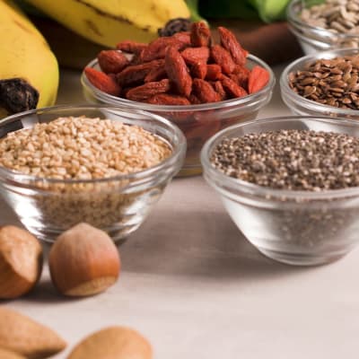 Superfoods auf grauem Hintergrund mit Platz für Text. Nüsse, Bohnen, Blattgemüse und Samen. Gesunde vegane Ernährung.
