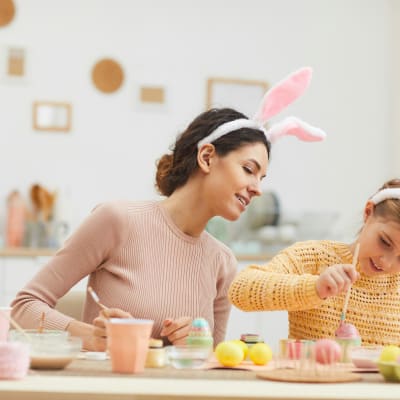 Eine Frau und ein Kind tragen Hasenohren und färben Ostereier