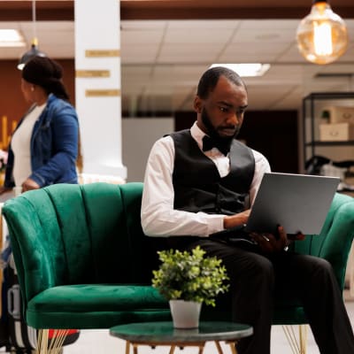  Der Hotelmanager sitzt in der Lobby, arbeitet an seinem Laptop, schaut auf den Bildschirm und behält den Überblick über die Buchungen.