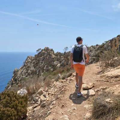 Entdecker durchquert atemberaubenden Klippenpfad mit Panoramablick auf den Ozean an einem Sommertag.