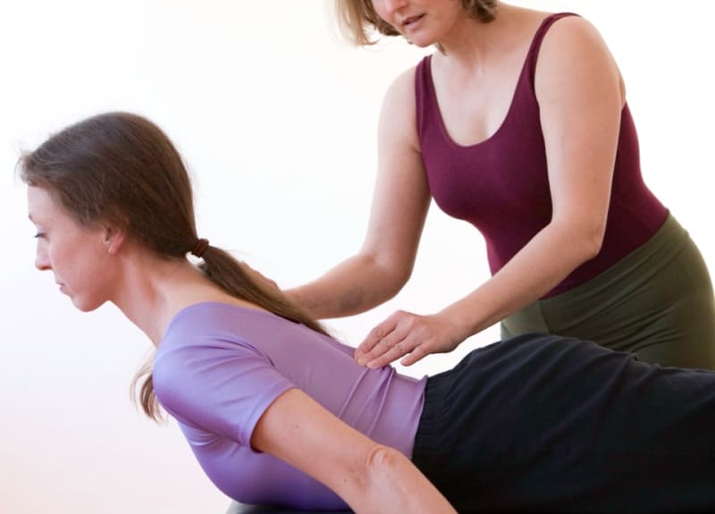 Die Trainerin korrigiert mit den Händen die Haltung einer Teilnehmerin auf der Matte | © Pilates Studio Hamburg / Sabine Büttner Photography