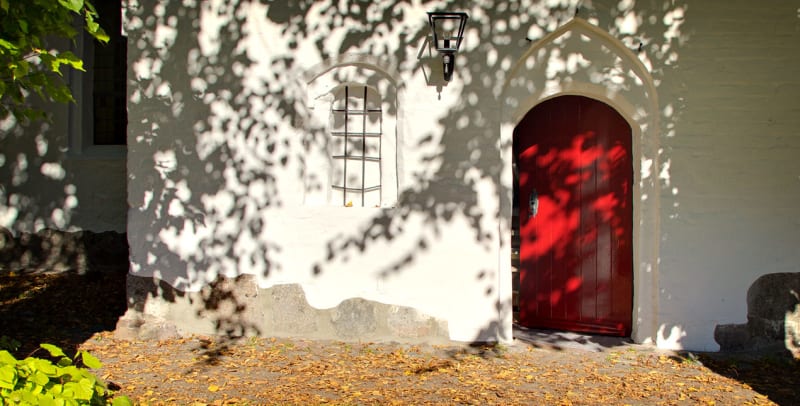 Rote Holztür und neu gestrichene Außenwand der Kirche Sieseby nach Aufarbeitung der Türen | © Malereibetrieb Jens Struck GmbH