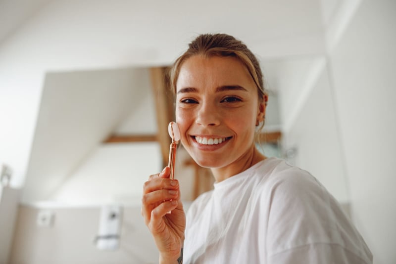 Junge Frau massiert ihr Gesicht mit einem Jadesteinroller im Badezimmer. Naturkosmetik-Konzept