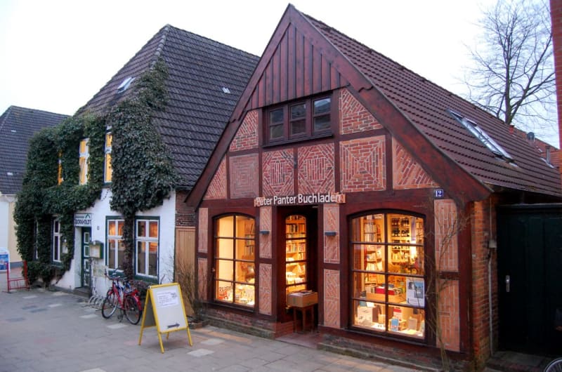 Außenansicht des Peter Panter Buchladens: das historische Fachwerkhaus in der Altstadt von Meldorf mit beleuchteten Schaufenstern am Abend | © Peter Panter Buchladen