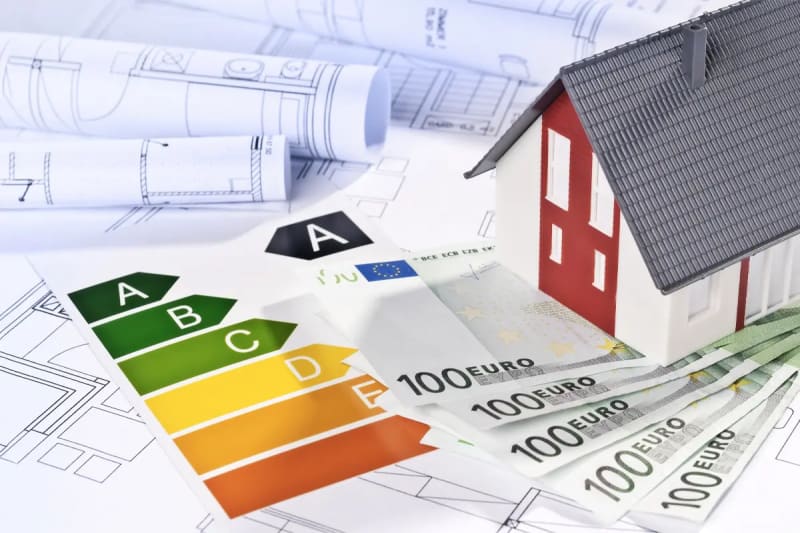 Hausmodell auf Bauplänen mit Energieeffizienzklassen und Euroscheinen als Symbol für Fördermittel bei der energetischen Sanierung | © Rüter Energieberatung