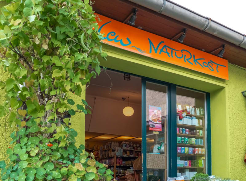 Eingang zum Lew Naturkostladen in Prenzlau mit orangefarbenem Schild und berankter Fassade | © Agentur Reichenberger