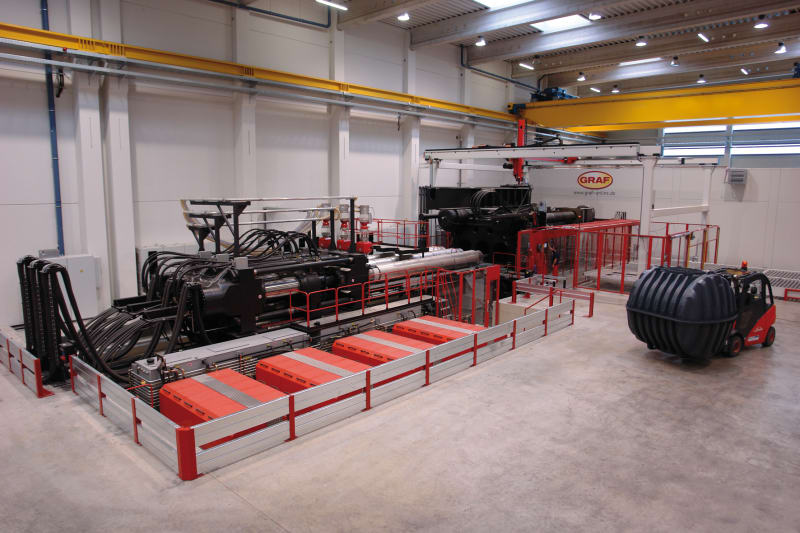 Produktionshalle der Otto Graf GmbH mit großer Spritzgießmaschine und fertigem Carat-Erdtank, der per Stapler transportiert wird