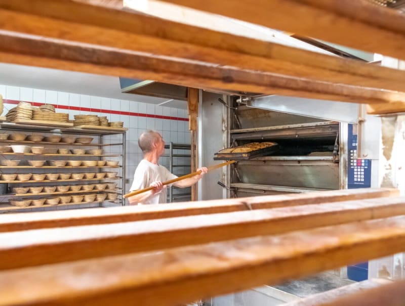 Bäcker schiebt Brote mit dem Brotschieber in den holzbefeuerten Backofen der Lew Biobäckerei | © Agentur Reichenberger