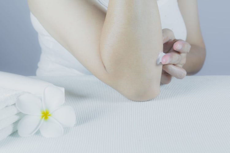 Die Hand einer Frau trägt mit einer Lotionsflasche Lotion auf die Haut ihres Arms auf.