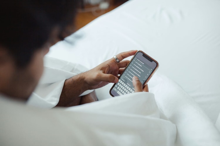 Person sitzt auf einem hellen Bett und tippt einen Chat auf dem Smartphone © Victoria Romulo / Unsplash+