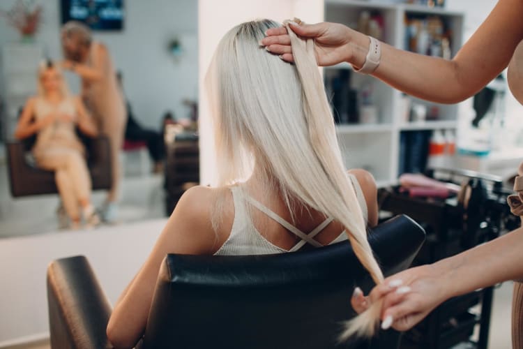 Eine Friseurin bringt einer jungen Frau mit blondem Haar in einem Schönheitssalon Haarverlängerungen an.