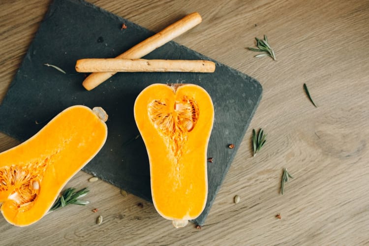 Vogelperspektive auf geschnittenen Butternut-Kürbis mit Kräutern und Brotstangen auf einem Schieferbrett. Pexels