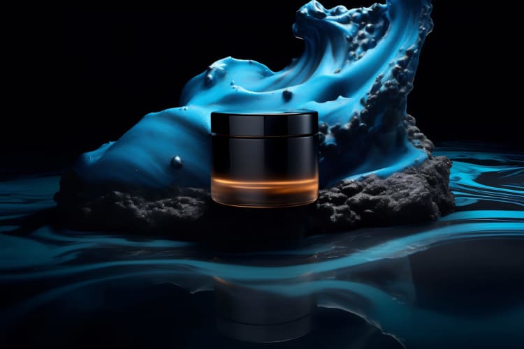 Nachtcreme fürs Gesicht in einem schwarzen Tiegel vor dem Hintergrund einer kunstvoll gestalteten blauen Gelwelle auf einer spiegelnden Oberfläche.