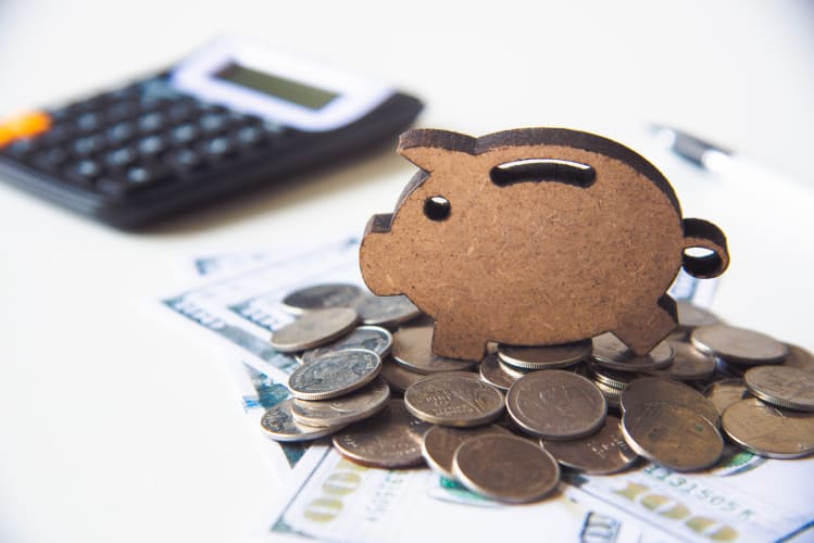 Sparschwein aus Holz mit Kleingeld und Taschenrechner im Hintergrund