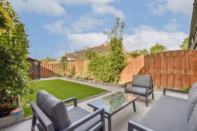 Eine schöne Gartenterrasse mit modernen Möbeln vor einer grünen Kulisse und einem Holzzaun. Ideal für Entspannung und Zusammenkünfte im Freien. null