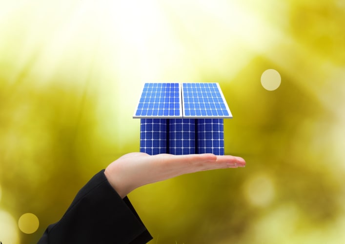 Ein haus aus Solarpaneelen  platziert auf einer Hand.
