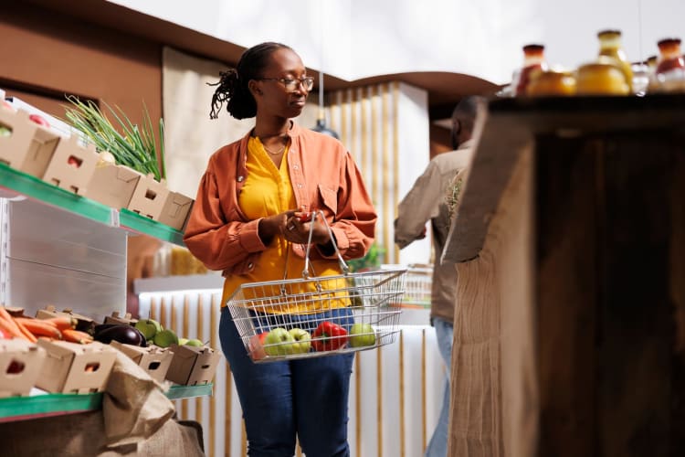 Eine Frau kauft in einem Öko-Supermarkt ohne Verpackung ein. Mit einem Einkaufskorb in der Hand durchstöbert sie eine Vielzahl frischer Bio-Produkte in Gläsern und achtet dabei auf nachhaltiges und gesundes Einkaufen.