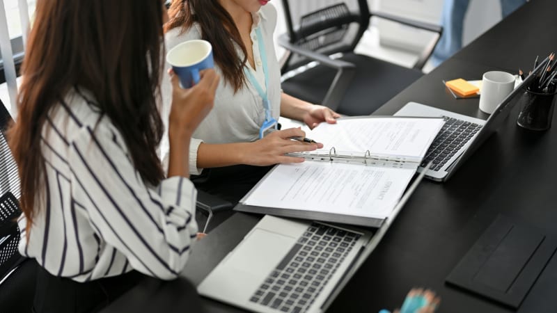 Zwei Frauen sitzen am Schreibtisch und blättern in einem Dokument null