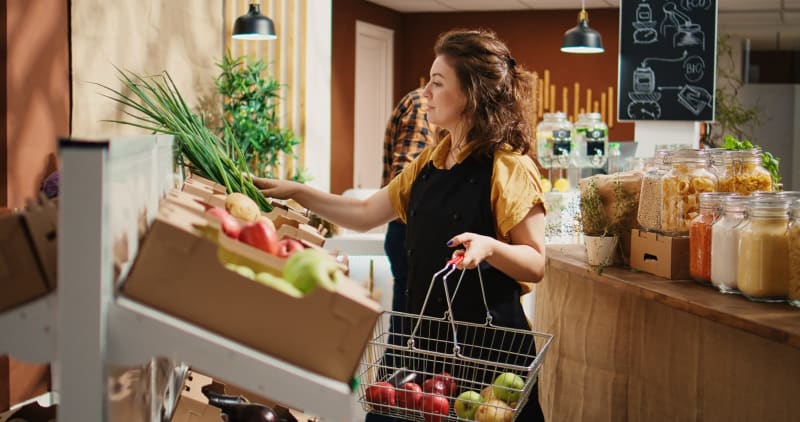 Ein fleißiger, umweltbewusster Mitarbeiter eines Lebensmittelladens füllt die Regale mit frischem Obst und Gemüse auf. Der Inhaber eines Supermarkts in der Nachbarschaft legt Lebensmittel aus biologischem Anbau in die Auslage.