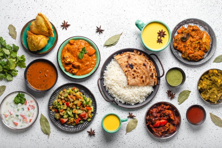 Indisches Buffet mit ethnischen Gerichten auf einem weißen Betontisch, von oben gesehen: Curry, Samosa, Biryani-Reis, Dal, Tofu Paneer, Chapatti, Naan, Chicken Tikka Masala, Mango-Lassi, indische Gerichte als Hintergrund für das Abendessen