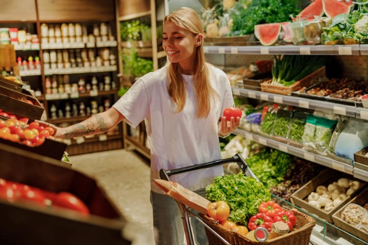 Eine Frau kauft heute vergnügt frisches und unverpacktes knackiges Obst und Gemüse in einem gut sortierten Supermarkt ein und genießt es.