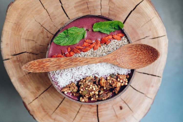 Gesunde Açaí-Schüssel mit Granola, Minzblättern und Beeren, serviert auf rustikalem Holz.