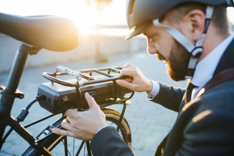Mann im Anzug und mit Fahrradhelm begutachtet den Akku seines E-Bikes  null