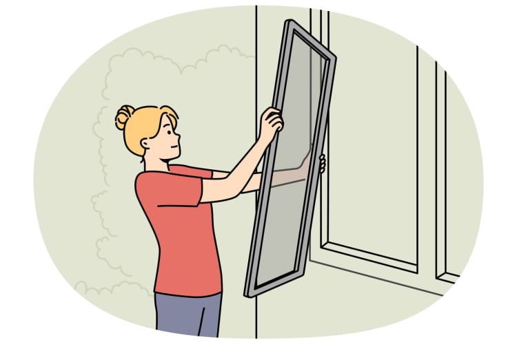 Frau montiert Fliegengitter an einem Hausfenster. null