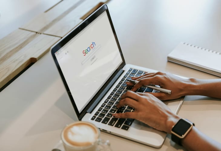 Frau tippt auf einem Laptop mit geöffneter Suchseite, daneben ein Kaffee © Curated Lifestyle / Unsplash+