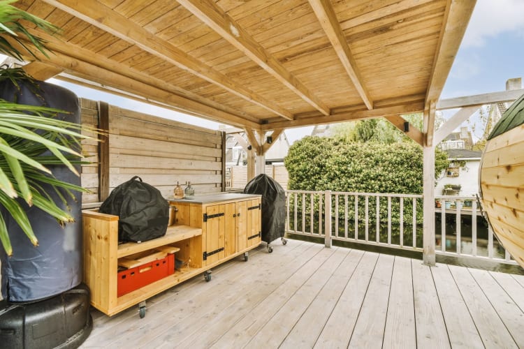 Ein Außenküchenbereich mit Holzboden und großen Topfpflanzen an der Seite der Terrasse mit Blick auf den Hinterhof. null