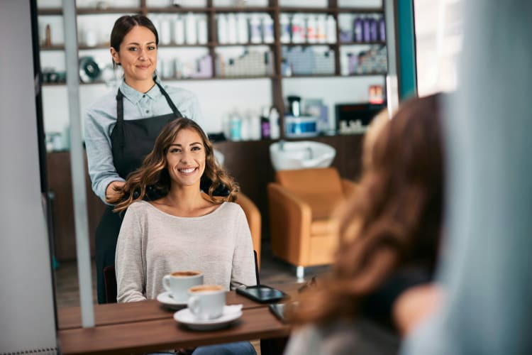 Junge Frau schaut zufrieden in den Spiegel und sitzt beim Friseur der ihre Haare stylt null