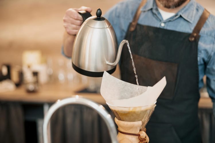 Barista mit einem Wasserkocher in der Hand, der kochendes Wasser durch einen Filter in eine Tasse gießt