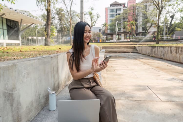 Eine fröhliche junge Frau nutzt ihr Smartphone und wirbt für einen nachhaltigen Lebensstil in einer wunderschönen Umgebung im Freien. null