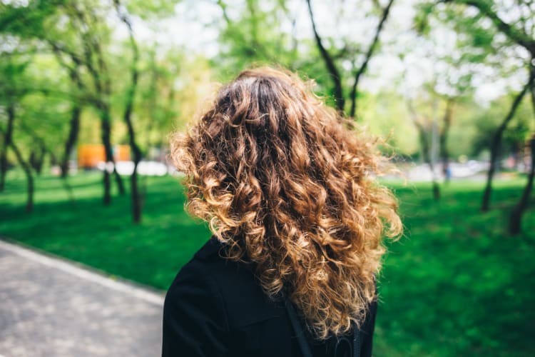 Frau von hinten mit lockigen schulterlangen mittelblonden Haaren progressman / shutterstock.com