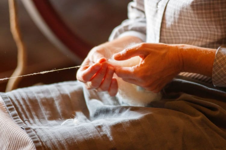 Die Hände einer Person, die Wolle mit traditionellen Methoden zu Garn spinnt.