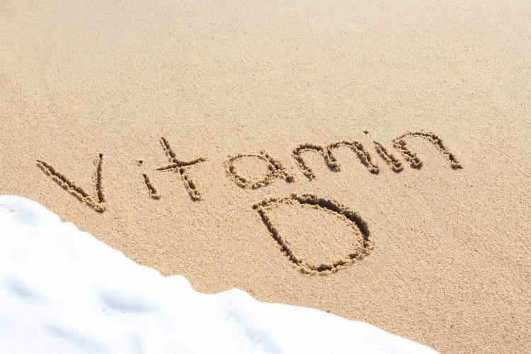 Vitamin D, geschrieben im Sand mit dem Schaum einer heranrollenden Welle null