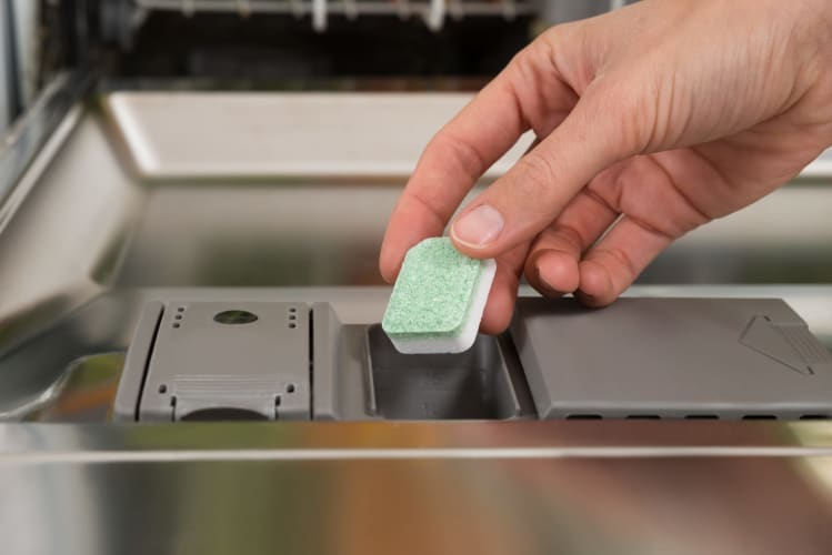 Nahaufnahme von Händen, die eine Spülmaschinentablette in das Spülmittelfach der Spülmaschine legen
