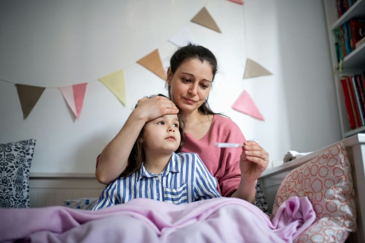 Mutter hält die Hand an die Stirn des Kindes und ein Thermometer in der anderen Hand null