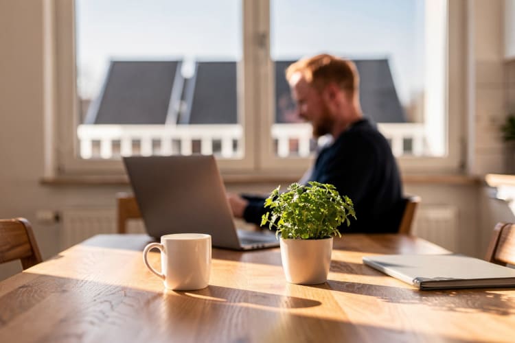 Mann am Laptop am Küchentisch, im Fenster dahinter Solarmodule am Balkongeländer KI-generiert