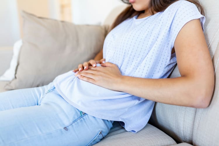 Frau mit Bauchschmerzen auf dem Sofa sitzend null
