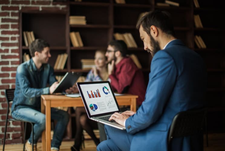 Der Finanzmanager der Geo-Sichtbarkeit haben will, arbeitet am Laptop an den Marketinggrafiken vor dem Hintergrund des Arbeitsbereichs des Geschäftsteams im Büro.