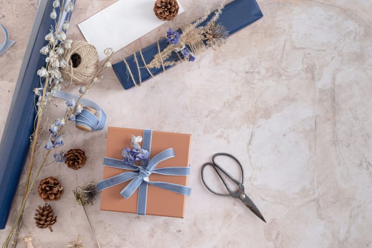 Geschenk, blaues SChleifenband Schere und Tannenzapfen liegen auf dem Boden null