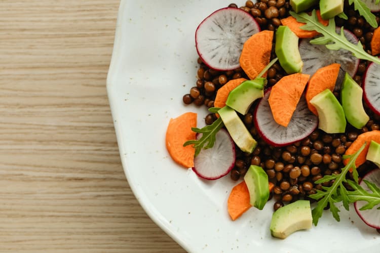 Linsen, Radieschen, Karotten und Avocado mit Rucola auf einem Teller null