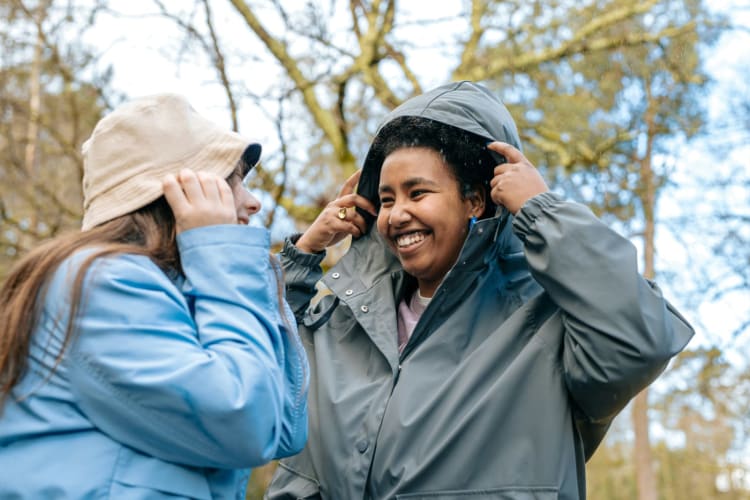 Zwei lachende Frauen in Regenjacken im herbstlichen Wald © A. C. / Unsplash+