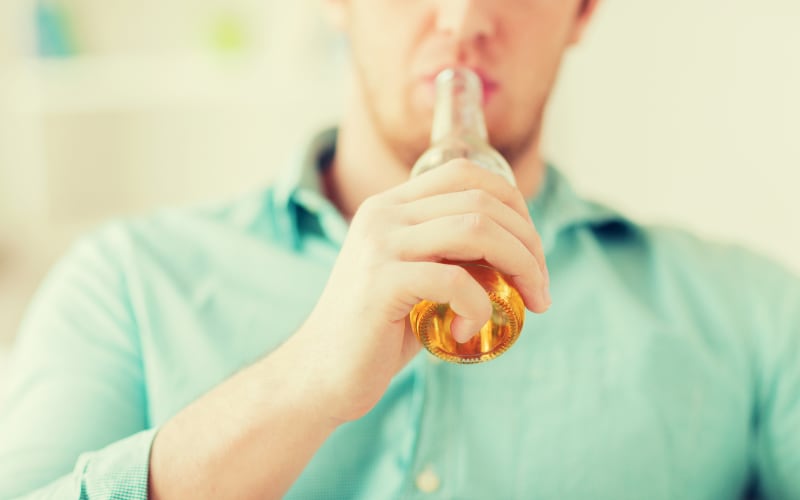Konzept: Getränke, Entspannung, Freizeit und Menschen – Nahaufnahme eines Mannes, der zu Hause auf dem Sofa sitzt und alkoholfreies Bier trinkt