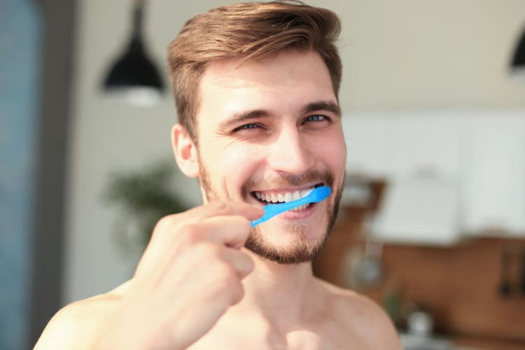 Junger Mann mit braunen Haaren, putz dich mit einer blauen Zahnbürste die Zähne.